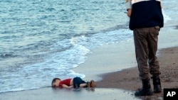 FILE - In this Sept. 2, 2015 photo, a paramilitary police officer investigates the scene before carrying the lifeless body of 3-year-old Aylan Kurdi from the sea shore, near the beach resort of Bodrum, Turkey.