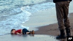 FILE - In this Sept. 2, 2015 photo, a paramilitary police officer investigates the scene before carrying the lifeless body of 3-year-old Aylan Kurdi from the sea shore, near the beach resort of Bodrum, Turkey.