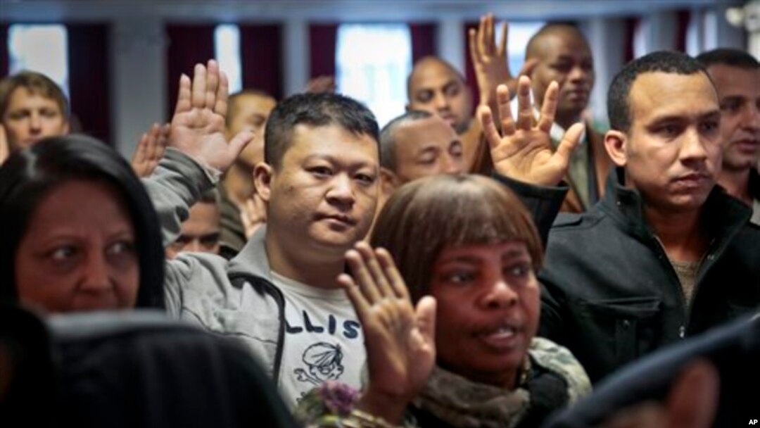 Inmigrantes alzan su mano para prestar juramento como nuevos ciudadanos estadounidenses en Nueva York.