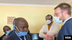 Detective Inspector Morgan Chafa (left) arguing with Doug Coltart of Zimbabwe Lawyers for Human Rights (right) while prominent journalist Hopewell Chin’ono (in PPEs) looks on July 21, 2020 in Harare. (VOA/Columbus Mavhunga) 