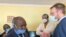 Detective Inspector Morgan Chafa (left) arguing with Doug Coltart of Zimbabwe Lawyers for Human Rights (right) while prominent journalist Hopewell Chin’ono (in PPEs) looks on July 21, 2020 in Harare. (VOA/Columbus Mavhunga) 