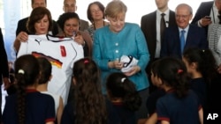 German Chancellor Angela Merkel (C) distributes shirts of the German national soccer team to Lebanese and Syrian displaced students studying together, during her visit to a Lebanese public school, in Beirut, Lebanon, June 22, 2018.