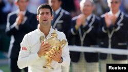 Novak Djokovic of Serbia reacts while holding the winner's trophy after defeating Roger Federer of Switzerland in their men's singles finals tennis match on Centre Court at the Wimbledon Tennis Championships in London July 6, 2014. 