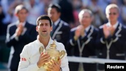 Novak Djokovic of Serbia reacts while holding the winner's trophy after defeating Roger Federer of Switzerland in their men's singles finals tennis match on Centre Court at the Wimbledon Tennis Championships in London July 6, 2014. 