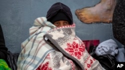 A migrant covers himself with blankets while waiting for help in downtown El Paso, Texas, Dec. 18, 2022.