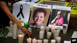 FILE - A woman places a candle in front of pictures of slain journalists Miroslava Breach, left, and Javier Valdez during a demonstration against the killing of journalists, outside the Interior Ministry in Mexico City, May 16, 2017.