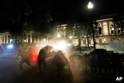 Protesters take cover from tear gas fired by police outside the Kenosha County Courthouse, late Monday, Aug. 24, 2020, in Kenosha, Wis.