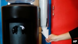 FILE - A faculty member gets a cup for bottled water at Gardner Elementary School in Detroit, Sept. 4, 2018. The Detroit school district will install hydration stations at all its schools after more than half tested positive for high levels of copper and lead in the water.