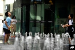 Boys spray water as they play in a fountain at a shopping and office complex in Beijing, Saturday, July 1, 2023. An orange alert, the second-highest level of warning, was issued for China's capital on Saturday as temperatures once again soared to around 40 degrees Celsius (104 degrees Fahrenheit) amid a weeks-long heat wave. (AP Photo/Mark Schiefelbein)