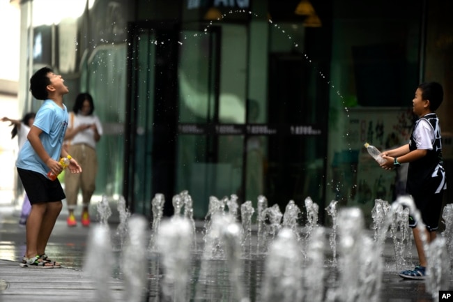 Boys spray water as they play in a fountain at a shopping and office complex in Beijing, Saturday, July 1, 2023. An orange alert, the second-highest level of warning, was issued for China's capital on Saturday as temperatures once again soared to around 40 degrees Celsius (104 degrees Fahrenheit) amid a weeks-long heat wave. (AP Photo/Mark Schiefelbein)