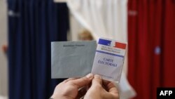 A polling station official holds an electoral card and a ballot at a polling station in Le Touquet, for the second round of the French regional elections on June 27, 2021. (Photo by Ludovic MARIN / Pool / AFP)