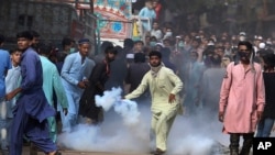 Supporters of Tehreek-e-Labiak Pakistan, a banned Islamist party, prepares to hurl back a tear gas canister fired by police to disperse protests over the arrest of their party leader Saad Rizvi, in Karachi, Pakistan, Monday, April 19, 2021.