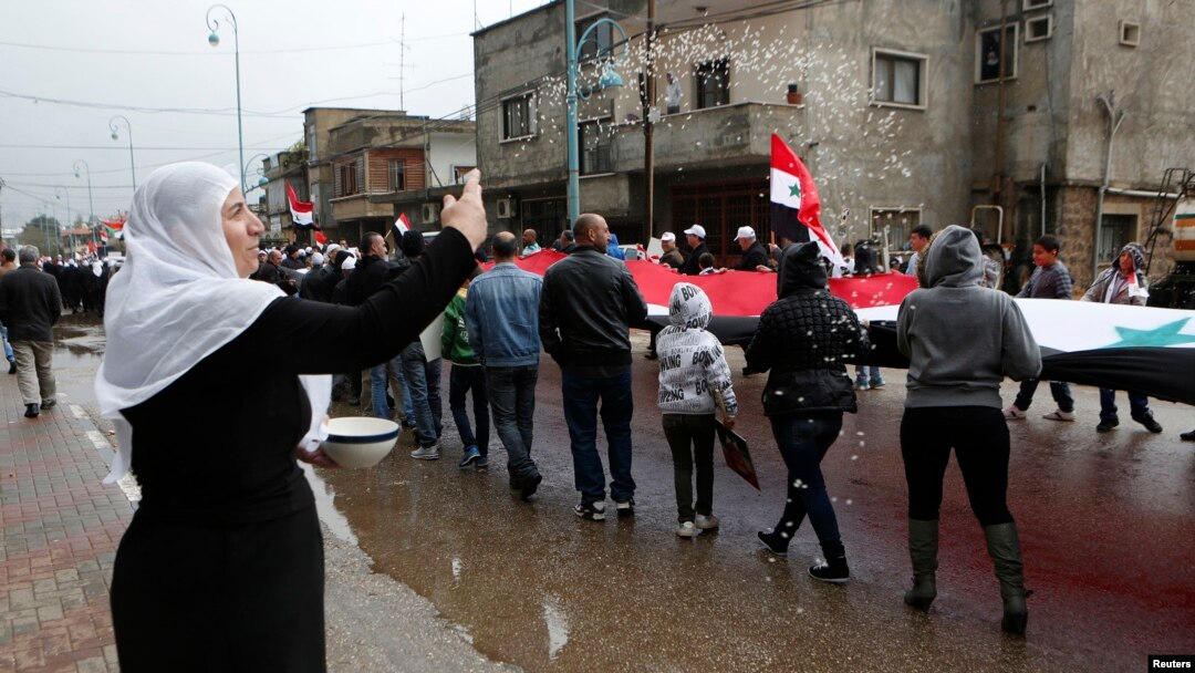 A woman throws rice as other members of the Druze community holding a Syrian flag walk past during a rally marking Syria's Independence Day in the Druze village of Buqata on the Golan Heights, April 17, 2013.