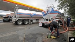 FILE - People wait in line as fuel is pumped from two tanker trucks at a convenience store in Wilmington, N.C., Sept. 17, 2018.