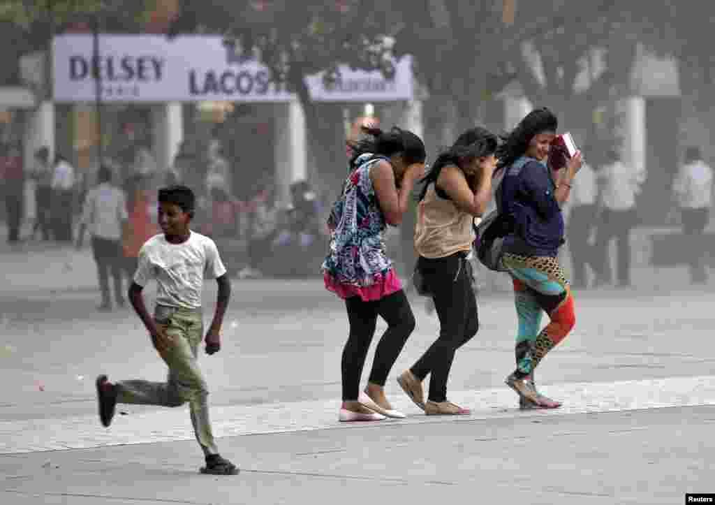 Seorang anak laki-laki berlari di samping para perempuan yang mencoba melindungi diri mereka dari badai debu di pusat perbelanjaan di Chandigarh, India.