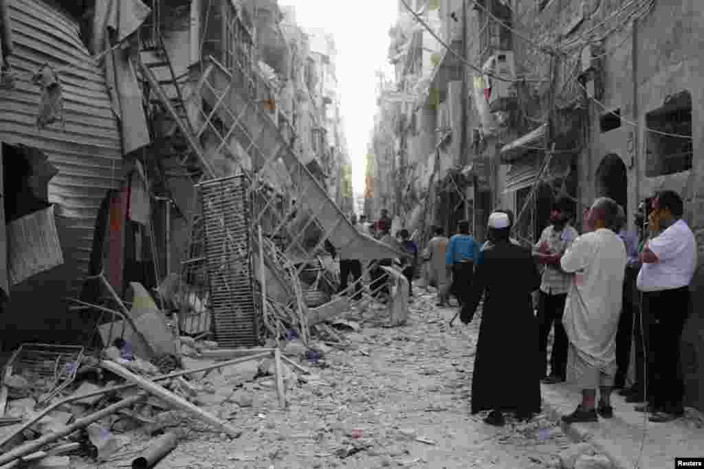 People stand near damaged buildings hit by what activists said was a barrel bomb dropped by forces loyal to President Bashar al-Assad, Bustan al-Qasr, Aleppo, May 28, 2014.