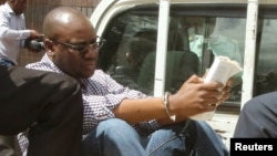 Zimbabwean Pastor Evan Mawarire reads a Bible as he arrives escorted by detectives at Harare Magistrates Court, Feb. 3, 2017.