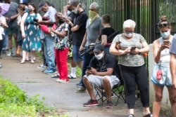 FILE - Steven Posey checks his phone as he waits in line to vote, June 9, 2020, at Central Park in Atlanta. Voters reported wait times of three hours.