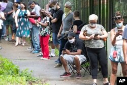 FILE - Steven Posey checks his phone as he waits in line to vote, June 9, 2020, at Central Park in Atlanta. Voters reported wait times of three hours.
