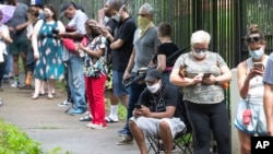 Steven Posey checks his phone as he waits in line to vote, Tuesday, June 9, 2020, at Central Park in Atlanta. Voters reported wait times of three hours. (AP Photo/John Bazemore)