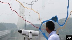 পানমুনজোমের কাছে উত্তর এবং দক্ষিণ কোরিয়ার মধ্যে সীমান্ত এলাকার একটি মানচিত্র দেখানো কাঁচের মধ্য দিয়ে এক ব্যক্তি উত্তর দিক দেখছেন। ৬ জুলাই, ২০১৭। ফাইল ছবি।.