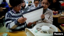 FILE - Students hold a HEPA filter as they prepare to put it on a fan at a workshop to learn how to make a DIY air purifier at a college in Beijing.