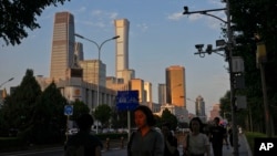 An evening sunlight casts on a woman as people walk near the Central Business District during the rush hour in Beijing on Monday, Aug. 14, 2023. (AP Photo/Andy Wong)