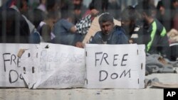 Seen through a wire fence, refugees and migrants most of them from Pakistan, hold placards during a third day of hunger strike to protest their deportation to Turkey, in the Greek island of Lesbos, April 7, 2016. 