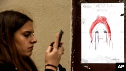 A woman checks her smartphone by a poster showing a weeping image of Marianne, symbol of the French Republic, near Le Carillon restaurant, a site of terrorist attacks, in Paris, Nov. 17, 2015. The attacks have triggered waves of social media communication