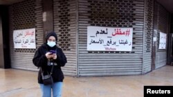 A woman walks past closed shopping center in Sidon, Lebanon, March 15, 2021. The Arabic reads: "Closed because we don't want to raise prices" and "Closed until the Lebanese Lira is rescued."