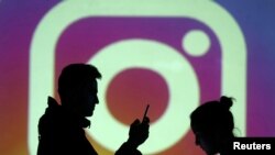 Las siluetas de los usuarios de dispositivos móviles se ven junto a una proyección en pantalla del logo de Instagram.