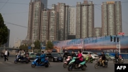 FILE - People ride electric bikes as they pass next to apartment buildings in Zhengzhou, Oct. 19, 2016.