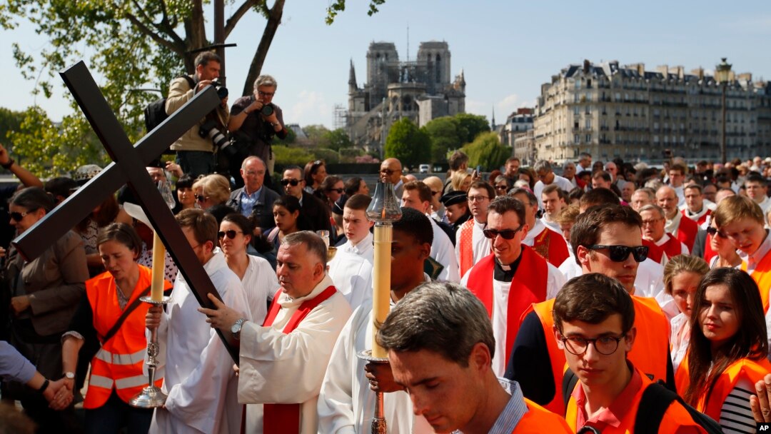 With Notre Dame cathedral in background, religious officials carry the cross during the Good Friday procession, in Paris, Apr. 19, 2019. 
