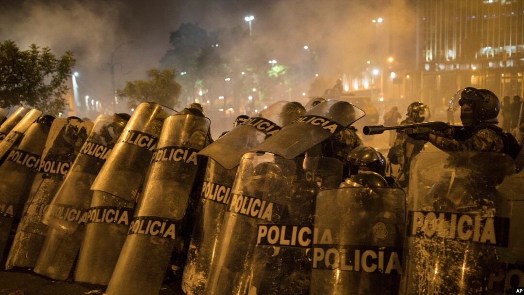 Police officers shield themselves from rocks thrown by protesters trying to march to Congress in a demonstration against the removal of President Martin Vizcarra, in Lima, Peru, Nov. 12, 2020. 
