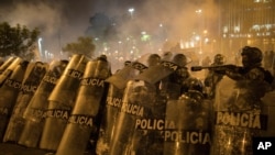 Police officers shield themselves from rocks thrown by protesters trying to march to Congress in a demonstration against the removal of President Martin Vizcarra, in Lima, Peru, Nov. 12, 2020. 