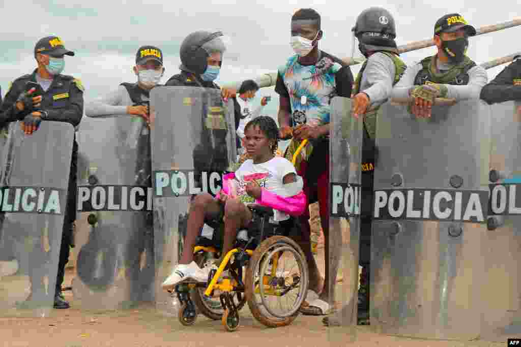 Police open the way to let through a woman in a wheelchair as a crowd of mixed nationality migrants attempt to cross into Peru on the Friendship Bridge along the border with Brazil, 1,600 kilometers southeast of Lima.