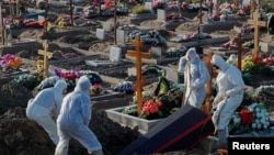 Grave diggers wearing personal protective equipment (PPE) lower a coffin while burying a person in the special purpose section of a graveyard for the coronavirus disease (COVID-19) victims on the outskirts of Saint Petersburg, Russia, Nov. 6, 2020.