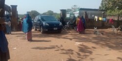 Some displaced women at the gate of the Durumi camp receive visitors who have come to donate supplies to them. January 1, 2020. (T. Obiezu/VOA)