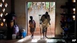 FILE - An elderly Muslim refugee uses crutches to walk next to a youth inside a Catholic church in Carnot, Central African Republic, April 2014.