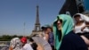 FILE - Stephanie Touissaint, foreground, uses a fan to keep cool in the sweltering heat at Eiffel Tower Stadium during a beach volleyball match between Cuba and Brazil at the 2024 Summer Olympics in Paris, July 30, 2024.