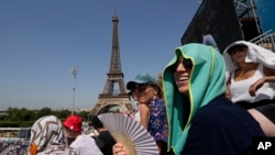 FILE - Stephanie Touissaint, foreground, uses a fan to keep cool in the sweltering heat at Eiffel Tower Stadium during a beach volleyball match between Cuba and Brazil at the 2024 Summer Olympics in Paris, July 30, 2024.