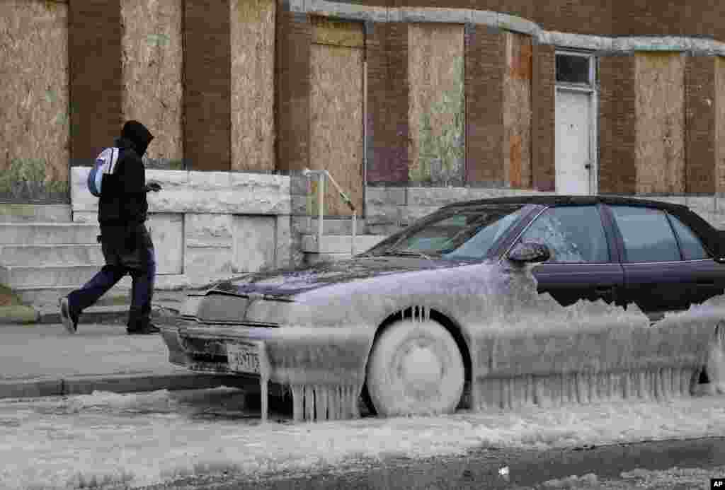 A man walks past a car partially covered in ice in Baltimore, Maryland, where temperatures continue to remain well below freezing. An arctic blast eased its grip on much of the U.S., with winds calming and the weather warming slightly a day after temperature records shattered up and down the Eastern Seaboard.