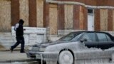 A man walks past a car partially covered in ice in Baltimore, Maryland, where temperatures continue to remain well below freezing. An arctic blast eased its grip on much of the U.S., with winds calming and the weather warming slightly a day after temperature records shattered up and down the Eastern Seaboard.