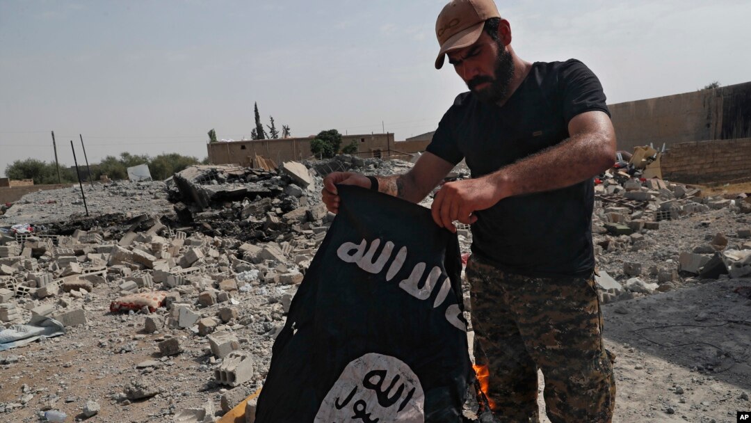 Seorang pejuang dari kelompok milisi Kristen Suriah membakar bendera ISIS di wilayah barat Kota Raqqa, di Suriah, pada 17 Juli 2017. (Foto: AP/Hussein Malla)