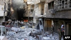 Syrian government forces walk down a destroyed street in the Hajar al-Aswad area on the southern outskirts of Damascus on May 21, 2018.