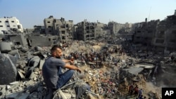FILE —A man sits on the rubble as others wander among debris of buildings that were targeted by Israeli airstrikes in Jabaliya refugee camp, northern Gaza Strip, Wednesday, Nov. 1, 2023.