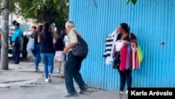 Una vendedora ambulante en el Centro Histórico de San Salvador se esconde de dos agentes metropolitanos que le prohiben acercarse con su venta a las plazas turísticas de la zona. [Fotografía: Karla Arévalo / VOA]