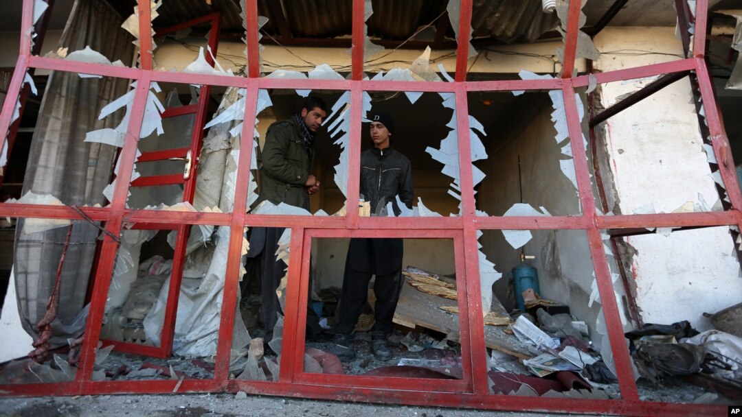 Seorang penjaga toko mengamati suasana di sekitarnya dari jendela tokonya yang hancur akibat serangan bom bunuh diri di Kabul, Afghanistan (28/12).