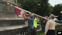 Para pekerja menurunkan bendera Konfederasi dari halaman gedung parlemen Alabama di ibukota Montgomery (24/6). (AP/Martin Swant)