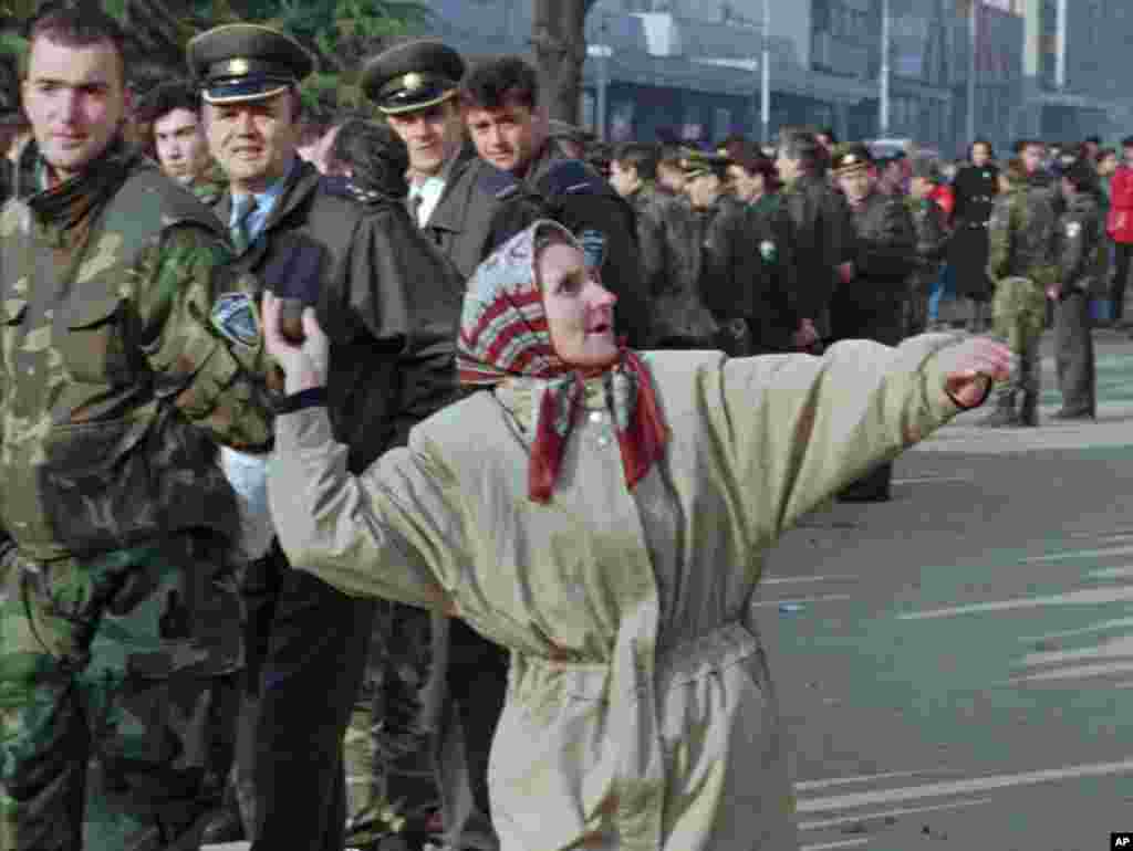 A woman from the eastern Bosnian enclave of Srebrenica throws a rock at the building where the Tuzla region officials are based, while policemen look on. (File 2006)